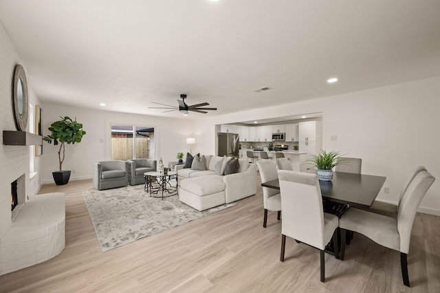 dining area featuring light wood-style flooring, a brick fireplace, visible vents, and baseboards