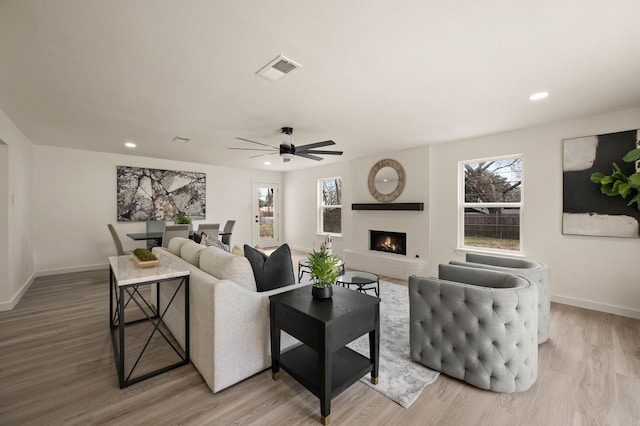 living area with visible vents, a brick fireplace, a healthy amount of sunlight, light wood-type flooring, and baseboards