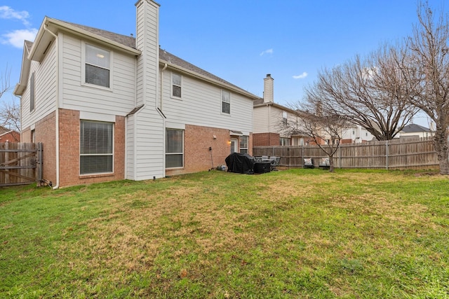 rear view of property featuring brick siding, a lawn, a chimney, and a fenced backyard