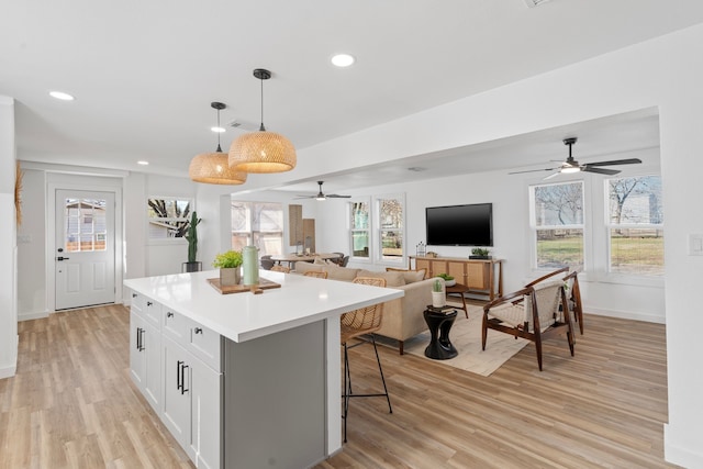 kitchen with a kitchen island, white cabinets, open floor plan, light countertops, and decorative light fixtures