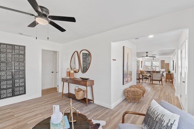 living area featuring baseboards, ceiling fan, visible vents, and light wood finished floors