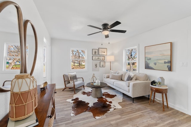 living room with light wood finished floors, a ceiling fan, and baseboards