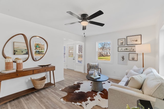 living area with light wood-style flooring, baseboards, and a ceiling fan