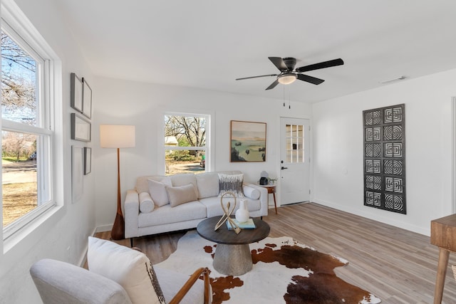 living area with visible vents, ceiling fan, light wood-style flooring, and baseboards