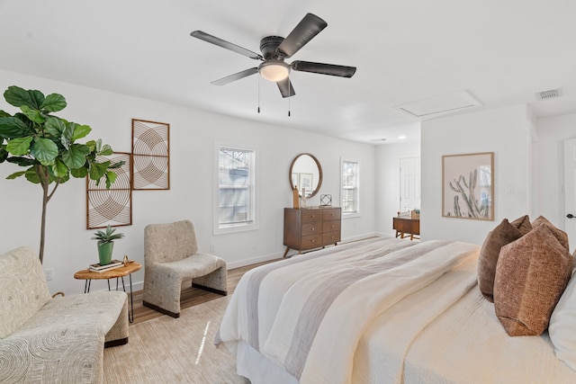 bedroom featuring ceiling fan, visible vents, baseboards, light wood finished floors, and attic access