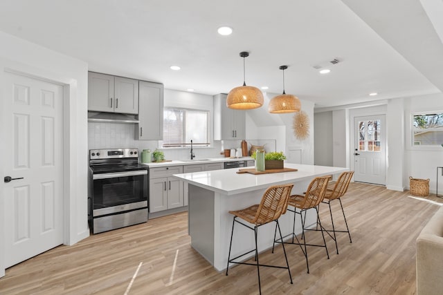 kitchen featuring a center island, decorative light fixtures, light countertops, electric range, and a sink