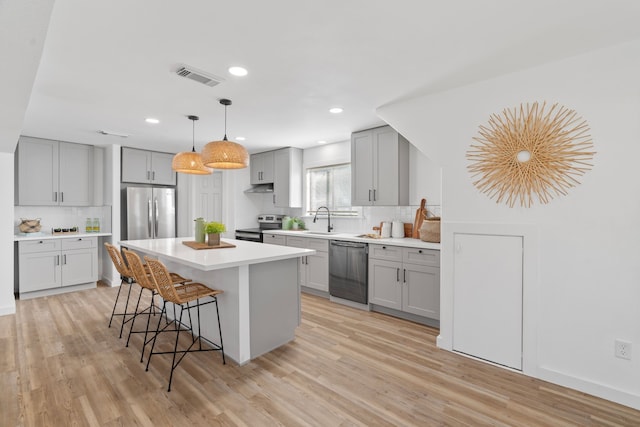 kitchen featuring visible vents, a kitchen island, stainless steel appliances, light countertops, and gray cabinetry