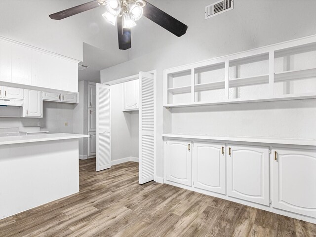 kitchen with under cabinet range hood, wood finished floors, visible vents, white cabinets, and light countertops