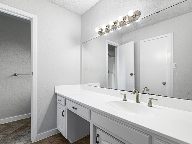 full bath featuring tile patterned floors, a textured wall, baseboards, and vanity