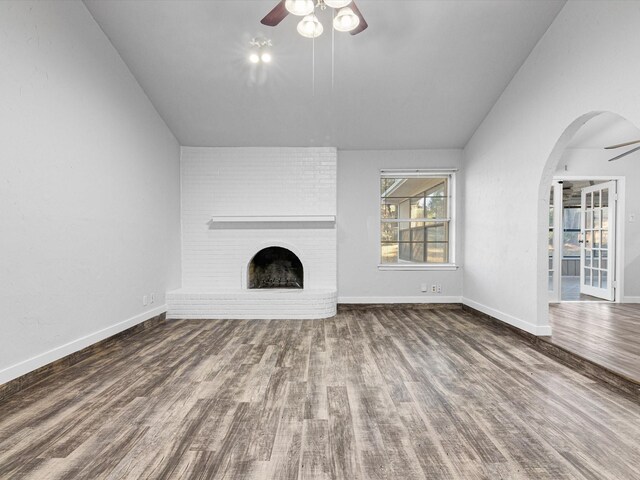 unfurnished living room with arched walkways, a ceiling fan, dark wood-style flooring, vaulted ceiling, and a brick fireplace