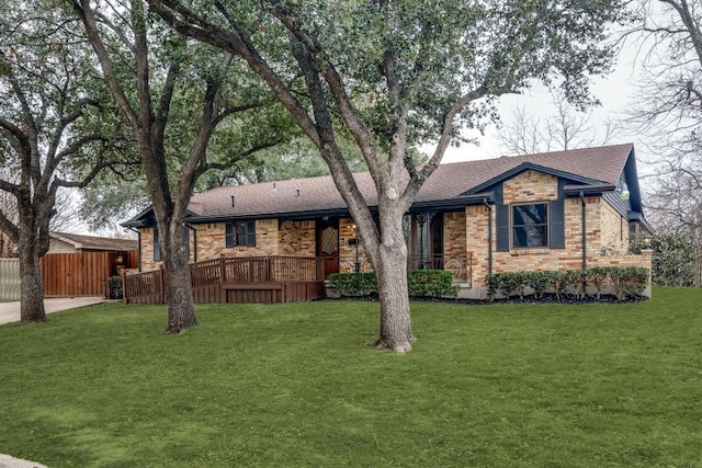 view of front of house featuring brick siding, roof with shingles, fence, a deck, and a front yard