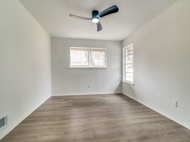 empty room featuring ceiling fan, visible vents, baseboards, and wood finished floors