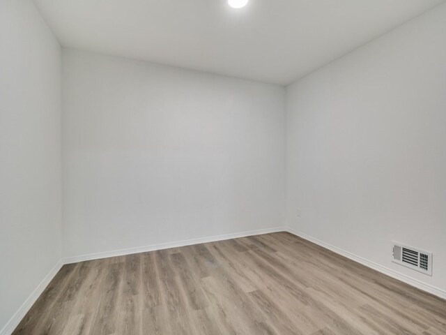 spare room featuring light wood-type flooring, visible vents, and baseboards