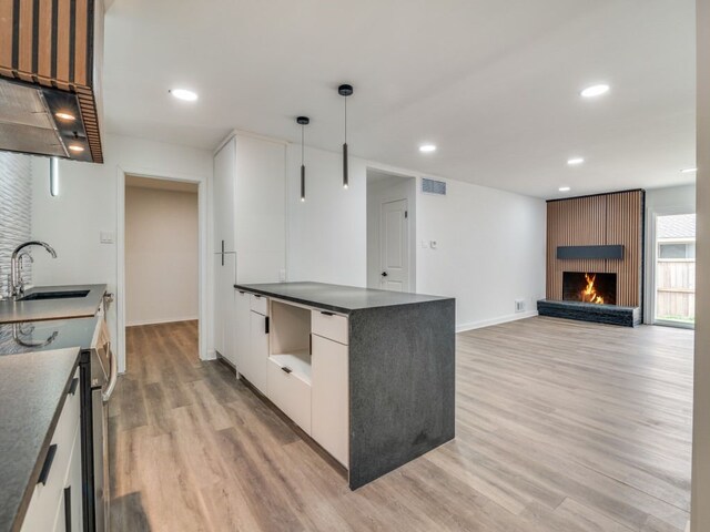 kitchen with dark countertops, visible vents, hanging light fixtures, white cabinets, and a sink