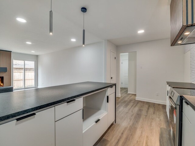 kitchen featuring stainless steel electric stove, dark countertops, hanging light fixtures, light wood-style floors, and white cabinets