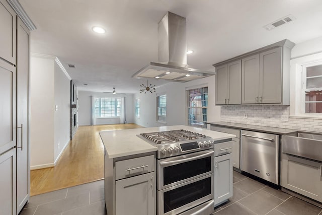 kitchen with gray cabinetry, stainless steel appliances, open floor plan, tile patterned floors, and island exhaust hood