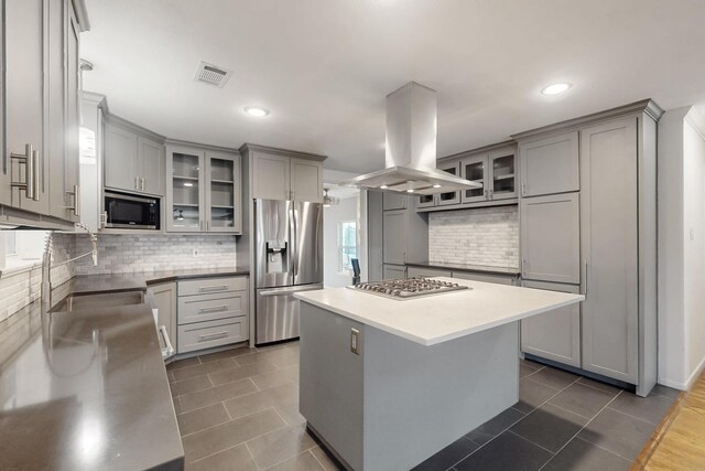 kitchen featuring appliances with stainless steel finishes, glass insert cabinets, island exhaust hood, and a kitchen island