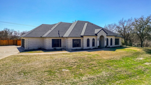 french country inspired facade featuring brick siding, fence, and a front yard