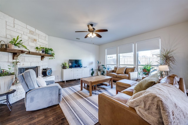 living area featuring a ceiling fan, visible vents, dark wood-type flooring, and a stone fireplace