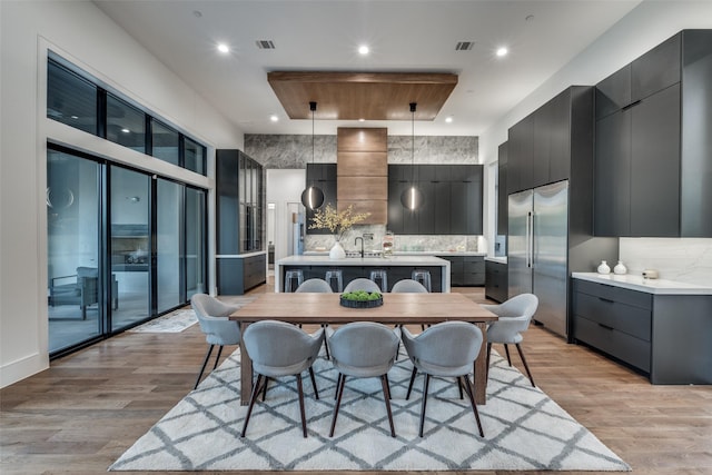 kitchen with decorative light fixtures, light countertops, stainless steel built in fridge, an island with sink, and modern cabinets