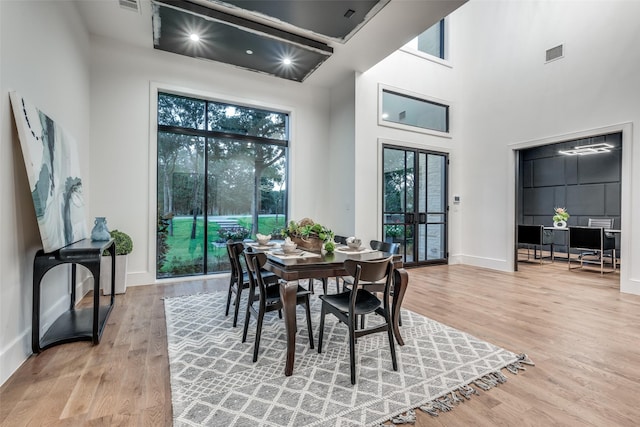 dining room featuring visible vents, light wood-style flooring, and a towering ceiling