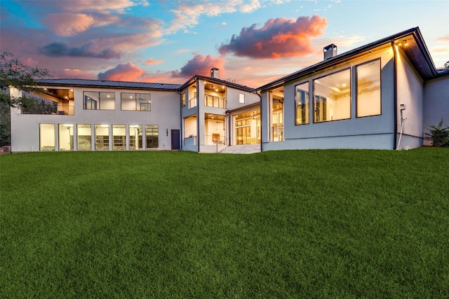 rear view of property with a standing seam roof, a chimney, and a yard