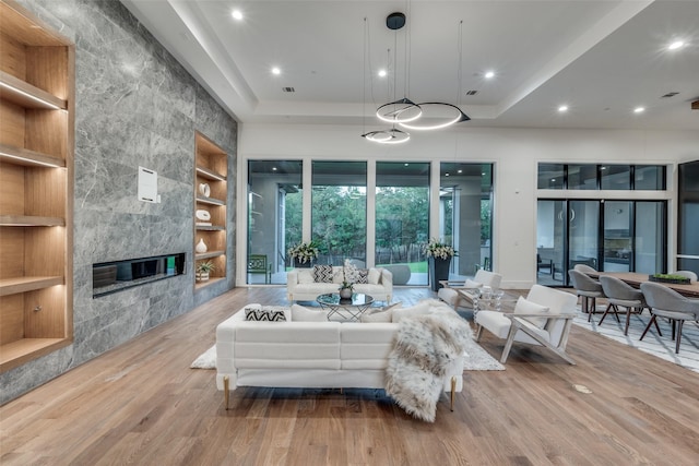 sunken living room featuring recessed lighting, a fireplace, light wood-style floors, built in features, and a tray ceiling