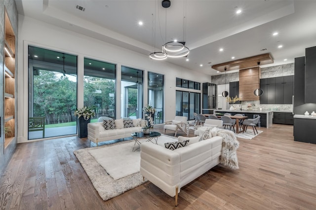 living room featuring a tray ceiling, visible vents, light wood-style flooring, and recessed lighting