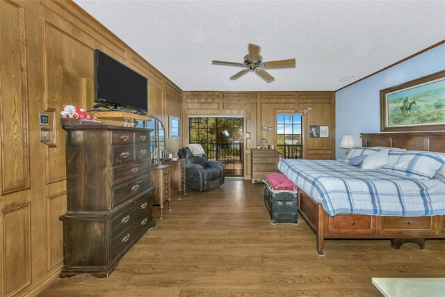 bedroom with access to exterior, crown molding, wood walls, a textured ceiling, and wood finished floors