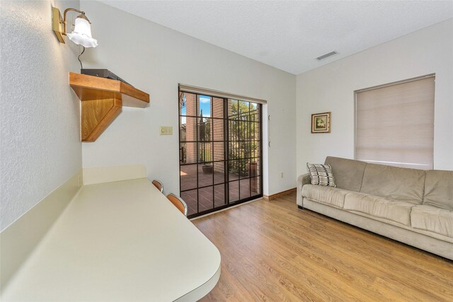 living room featuring baseboards, light wood-style flooring, visible vents, and a textured ceiling