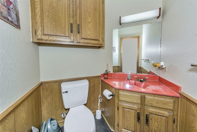 half bathroom with a wainscoted wall, a textured wall, toilet, wooden walls, and vanity