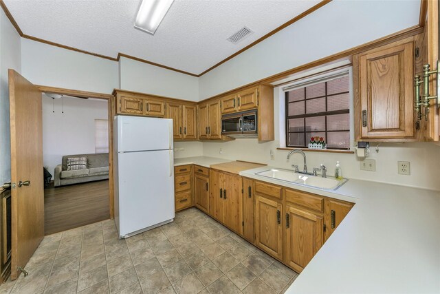 kitchen featuring black microwave, visible vents, light countertops, freestanding refrigerator, and brown cabinets