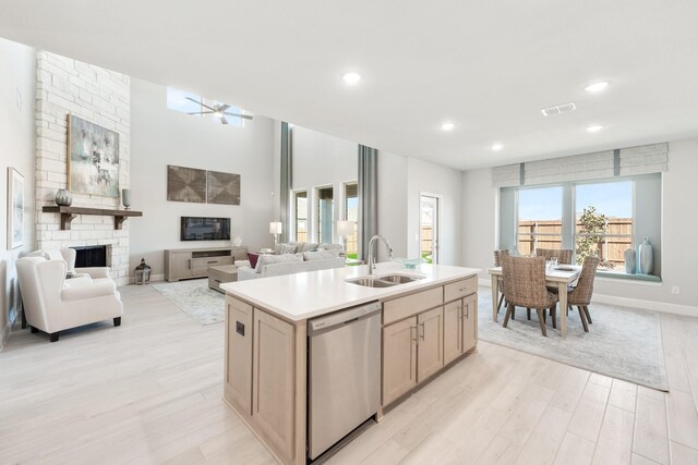 kitchen featuring open floor plan, light countertops, stainless steel dishwasher, a fireplace, and a sink