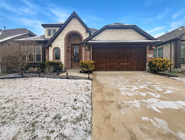 french country home featuring an attached garage, stone siding, concrete driveway, and brick siding