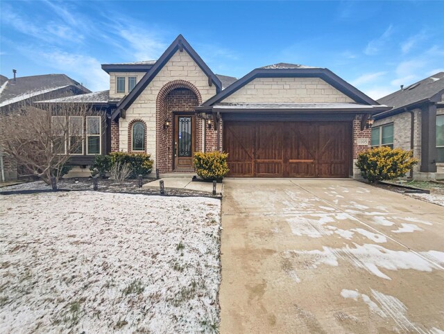 french country home with driveway, brick siding, and an attached garage