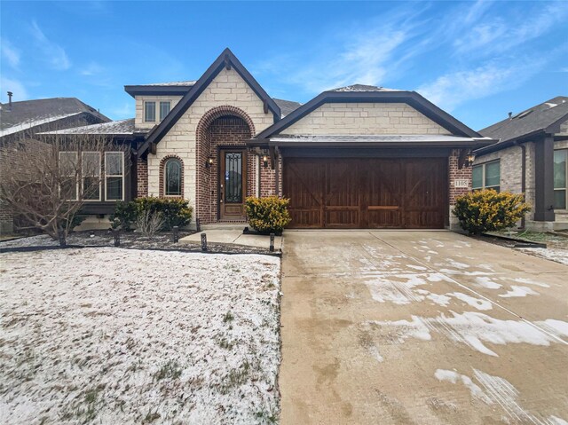 french country style house featuring an attached garage, concrete driveway, and brick siding