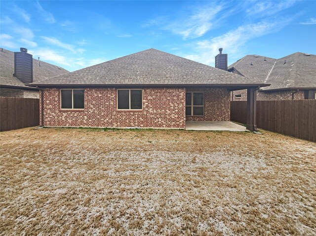 rear view of property featuring a shingled roof, a fenced backyard, a patio, and brick siding