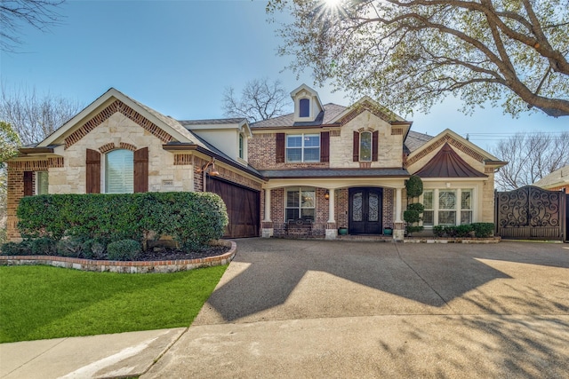 view of front of property featuring driveway, stone siding, an attached garage, french doors, and brick siding