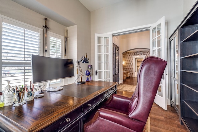 home office with arched walkways, french doors, and dark wood-style floors