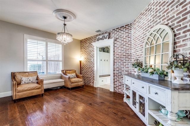 living area featuring visible vents, baseboards, brick wall, dark wood-type flooring, and a notable chandelier