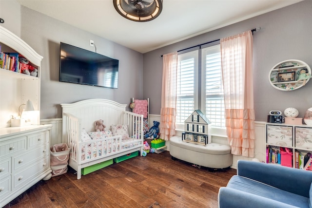 bedroom featuring a nursery area, dark wood-type flooring, and wainscoting