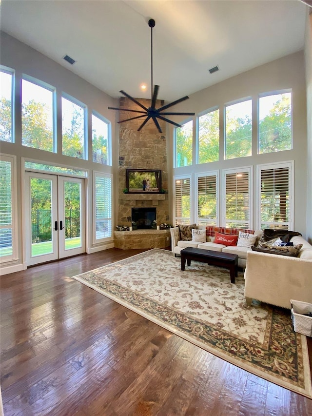 living area featuring french doors, a fireplace, visible vents, a towering ceiling, and wood finished floors