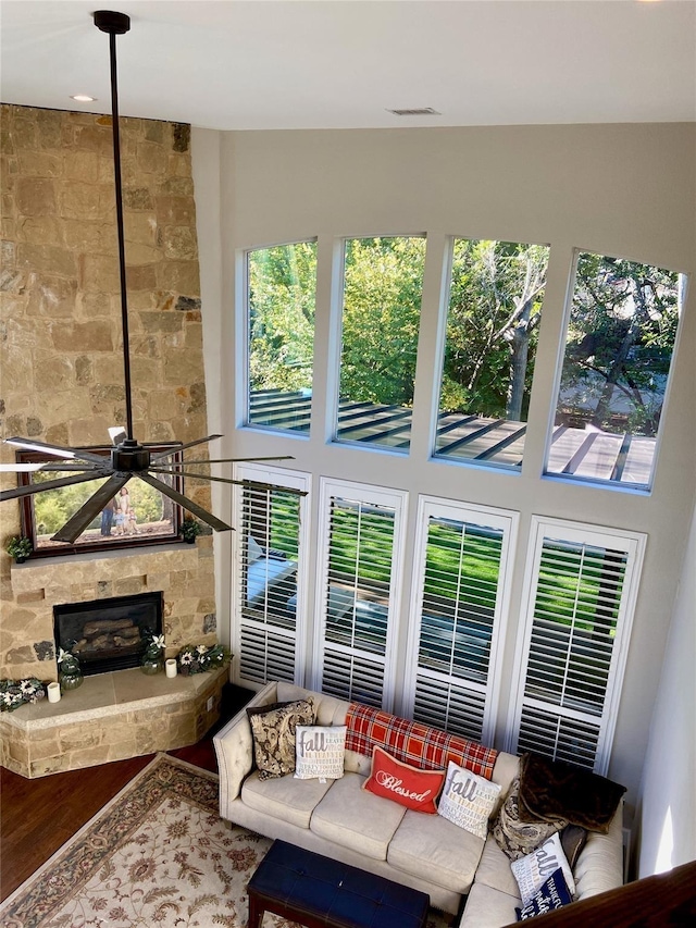 living room with a fireplace, visible vents, a high ceiling, a ceiling fan, and wood finished floors