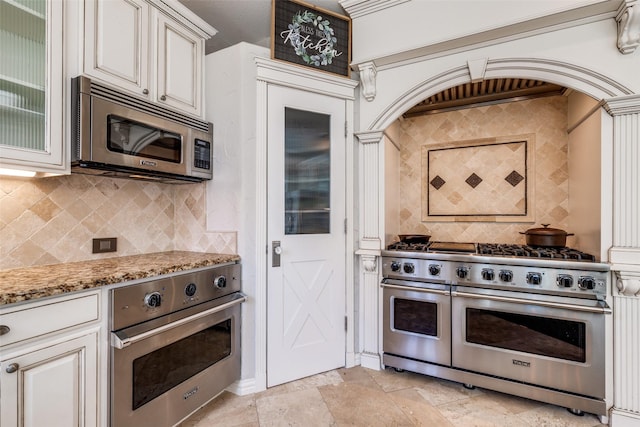 kitchen with appliances with stainless steel finishes, stone tile floors, decorative backsplash, and light stone countertops