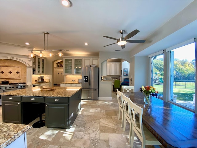 kitchen featuring a center island, arched walkways, hanging light fixtures, glass insert cabinets, and high quality appliances