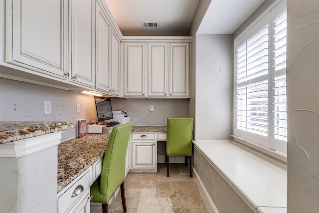 office area featuring a healthy amount of sunlight, visible vents, stone tile flooring, and built in study area