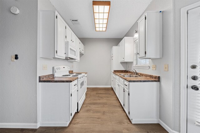 kitchen featuring white appliances, a sink, visible vents, white cabinetry, and dark countertops