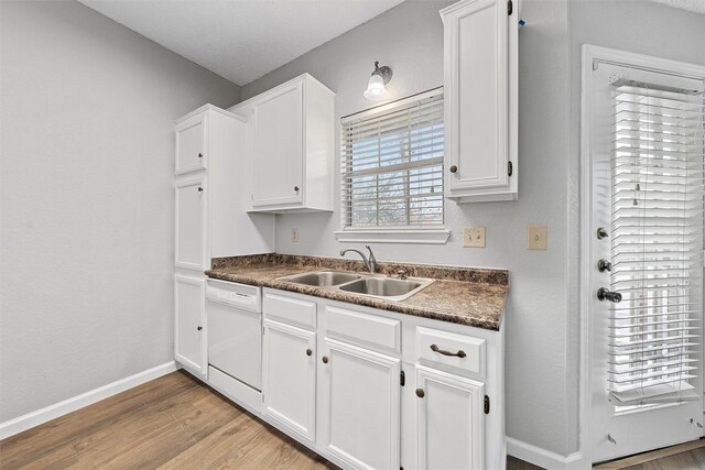 kitchen with a sink, white cabinets, dishwasher, light wood finished floors, and dark countertops