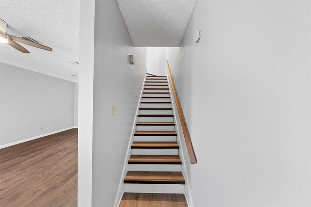 stairs with a textured ceiling, wood finished floors, a ceiling fan, and baseboards