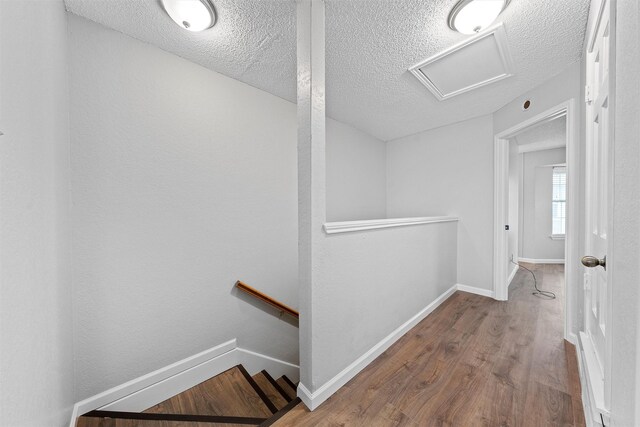 hall featuring attic access, baseboards, wood finished floors, and an upstairs landing